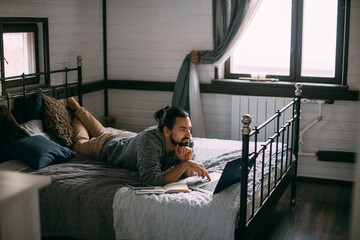 Fototapeta premium Young man lies on bed with laptop at home