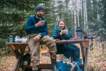 Man and woman hikers drink tea at a halt in the forest.
