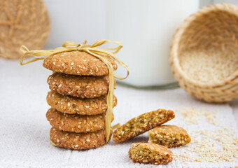 Stack of sesame cookies, sesame seeds in a wicker basket on rough woven tablecloth