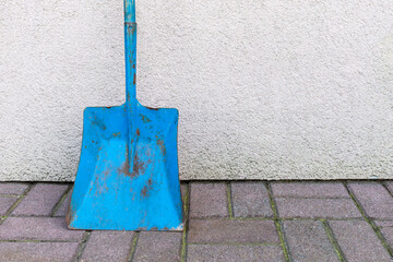 Grunge vibrant blue shovel (spade) standing near the wall outside the house or garage
