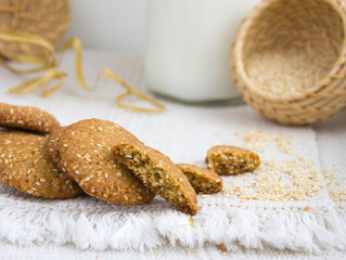 Sesame cookies on a white plate, sesame seeds in a wicker basket, rough woven tablecloth