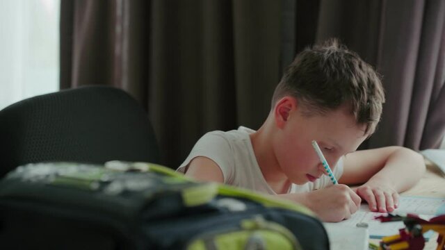 a capable student of 8 years old, writes in a notebook at the table.  the boy is doing his homework. Home schooling.