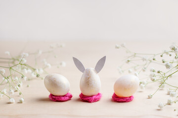 Miniature egg in the shape of a rabbit on a pink stand. Postcard with flowers for the holiday of Easter. Horizontal photo with place for text.