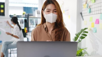 Asia businesswoman wear face mask for social distancing in new normal situation for virus prevention while using laptop presentation to colleagues about plan in video call while work in office. - Powered by Adobe