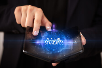 Naklejka premium Young man holding a foldable smartphone with ACADEMIC STANDARDS inscription, educational concept
