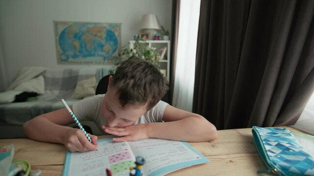a capable student of 8 years old, writes in a notebook at the table.  the boy is doing his homework. Home schooling.