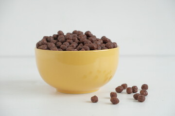 Chocolate cereal corn balls in a yellow bowl scattered on a white background. Copy, empty space for text