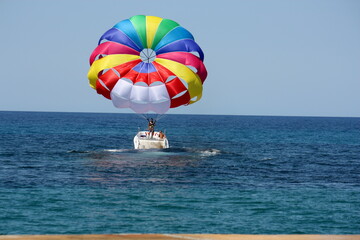 różnokolorowy, tęczowy spadochron ciągnięty przez motorówkę na tle lazurowego morza śródziemnego