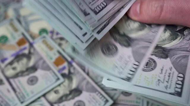 A man's hands are counting a thick stack of dollars against a background of scattered $ 100 bills. Concept of investment, success, financial prospects.