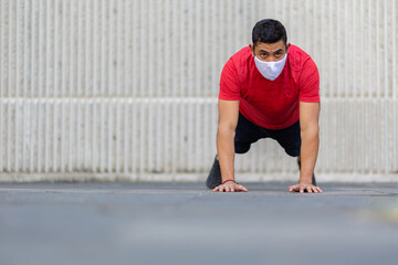 Mexican man doing push ups outdoors wearing a white face mask