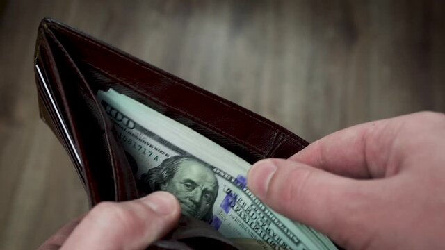 A man's hands open a wallet filled with 100 dollar bills and pass one bill to someone.