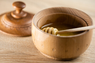 honey in a deep wooden bowl, rustic wooden plate. The wooden spoon drips slowly.