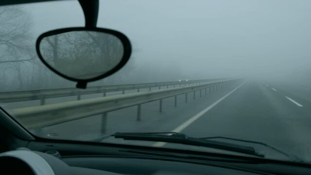 View through windshield from driving auto in highway on foggy day.Poor road visibility.Cloudy gray weather. View from passenger seat to moving oncoming traffic, bump stop,asphalt, white dividing line