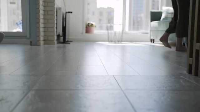 Close-up, male feet in socks and bare female feet walk in different directions on tiles of apartment. Man catches up with woman