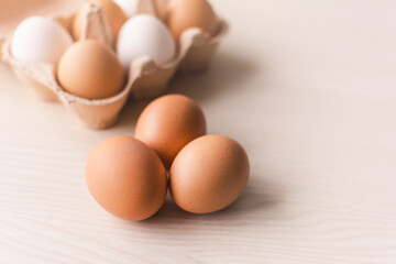 Three raw chicken eggs on a wooden table with a group of eggs in a box on the background.