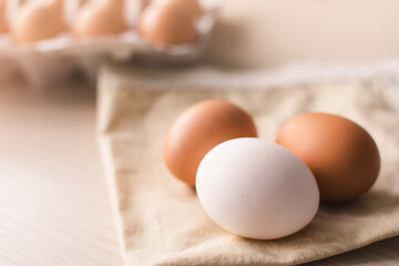 Three raw chicken eggs on a cloth bed with a group of eggs in a box on the background.