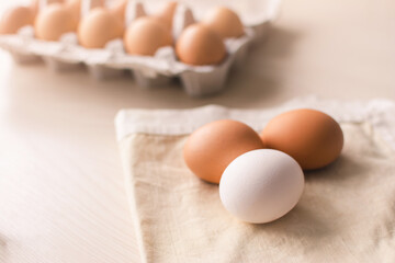Three raw chicken eggs on a cloth bed with a group of eggs in a box on the background.