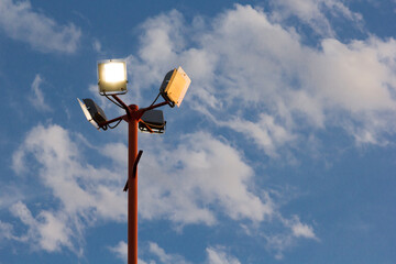 Poste de luz con varios reflectores con fondo de cielo nuboso
