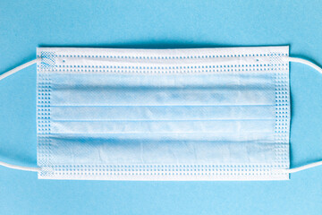 Blue surgical mask on light blue background. Disposable hygienic mask against Coronavirus Covid-19. Protection against flu, respiratory virus, air pollution. Healthcare during viral pandemic. Flat lay