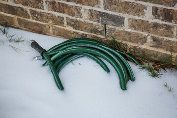 Green garden hose buried under ice and snow after winter storm