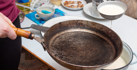The dough for pancakes is collected with a ladle and poured into a frying pan. Preparation for the celebration of Maslenitsa. Selective focus.