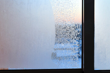 Winter. Cold. Frozen window with a beautiful frosty pattern in the form of snowflakes. The pink dawn is visible through the glass.