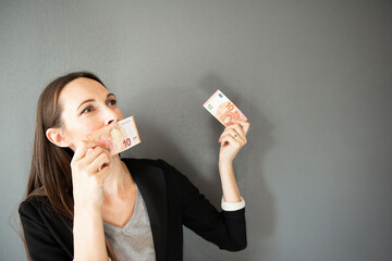 Portrait of business woman holding 10 euro bills on gray background. Female kissing euro in her hand