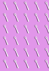 Vertical pattern with white disposable forks with a shadow on a lilac background.