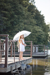 A beautiful girl of six years old in a short white dress stands on the masonry near the river and...