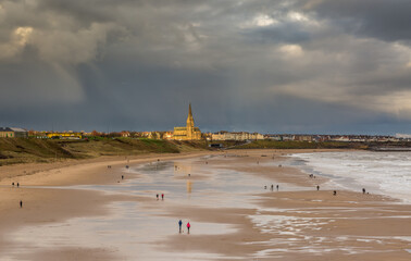 Fototapeta premium People taking a walk on Tynemouth's Longsands beach during Lockdown on a cloudy and rainy day, in the north east of England