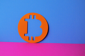 An orange bitcoin coin on a blue background and a pink table with a copy space. Conceptual collage about cryptocurrency in the style of cyberpunk and minimalism. High quality photo