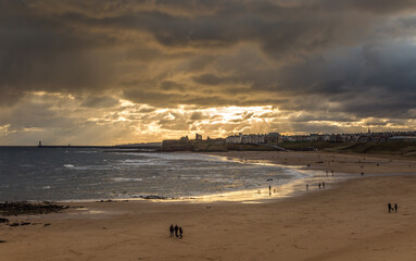 People taking a walk on Tynemouth's Longsands beach during Lockdown on a cloudy and rainy day, in the north east of England