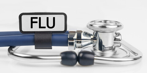 On the white surface lies a stethoscope with a plate with the inscription - FLU