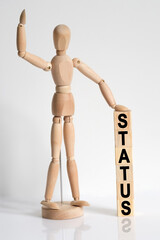 The wooden man raised his hand, and under his left hand he has cubes with the inscription - STATUS