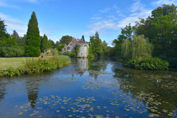 Fototapeta na wymiar A woman admiring the exterior of a British medieval castle and its reflection in water Exotic gardens with panoramic views of a moated fortress and a Victorian country mansion all in a historic estate