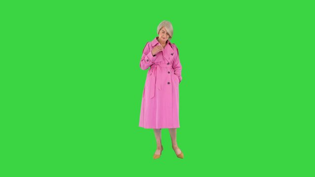 Trendy beautiful senior woman in a pink coat walks in and showing her outfit to camera on a Green Screen, Chroma Key.