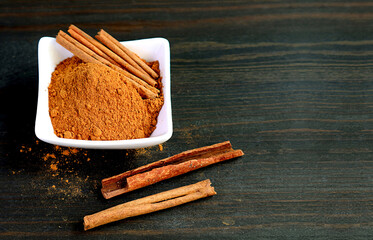 Bowl of ground cinnamon powder with cinnamon stick on black wooden background