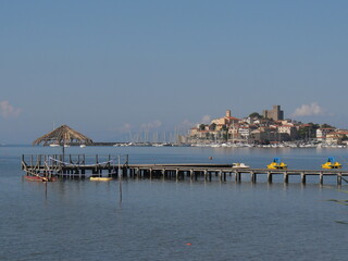 Panorama of the fortified medieval village of Talamone and of its coast lapped by the Tyrrhenian Sea with a wooden pier.