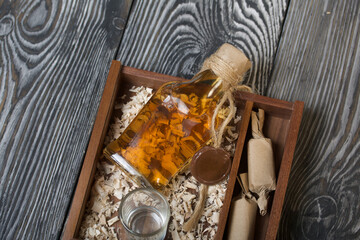 Fototapeta na wymiar Gift alcohol. A bottle of alcohol and candy are in a wooden box. On wood sawdust. Close-up shot.
