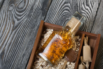 Fototapeta na wymiar Gift alcohol. A bottle of alcohol and candy are in a wooden box. On wood sawdust. Close-up shot.