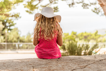 Obraz premium child with beautiful blond hair and white hat sitting in stairs and looking to the sea and the city