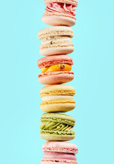 Stacking on pile Different types Sweet and colorful french macarons on blue background with copy space. Food Mockup for the holiday invitation card.