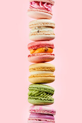 Stacked on top of each other different types sweet and colorful french macarons on pink background. Food mockup for the holiday invitation card.
