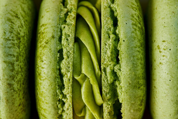 Macro plan of green French macaroons with matcha flavor. Close up of the cream filling with different toppings and fluffy cookies.
