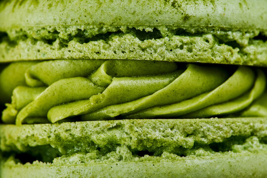 Macro plan of green French macaroons with matcha flavor. Close up of the cream filling with different toppings and fluffy cookies.