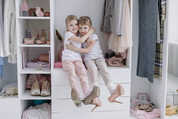 Family wardrobe. Happy twin sisters on shelve in closet with natural organic clothes in cozy...