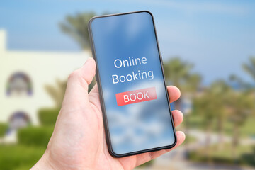 Hand holds phone with concept of online booking against the background of the hotel