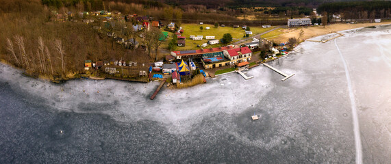 Zimowy krajobraz w miejscowości Długie, widok z lotu ptaka na jezioro skute lodem i brzeg głównej plaży jeziora Lipie, lubuskie - obrazy, fototapety, plakaty