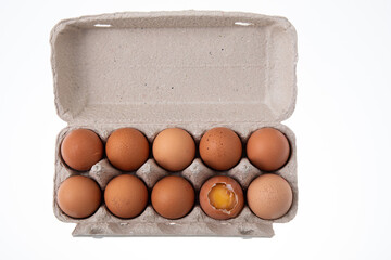 Top view of ten raw chicken eggs in egg box with one egg cracked