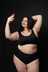 Plus size model in lingerie, fat sexy woman in underwear on black studio background, body positive concept, full length portrait.Girl model plus size takes a selfie